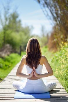 Young woman doing yoga in nature. Female wearing white sport clothes in lotus figure.