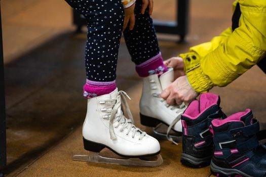 Family in a winter park. Mother with daughter in a ice arena. Mom puts her daughter in skates