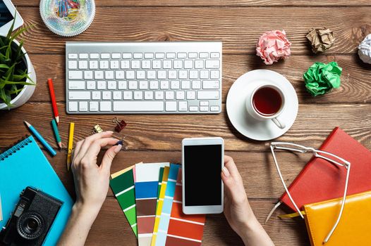 Web designer choosing colors from swatches at wooden desk. Top view office workplace with computer keyboard and stationery. Designing user interface of mobile application. Coloristics in visual design