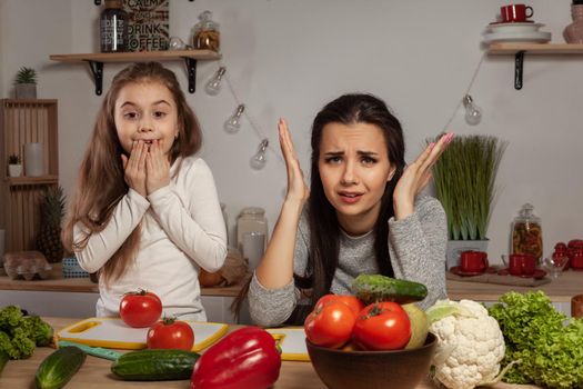 Happy loving family are cooking together. Lovely mom and her kid are making a vegetable salad and tired of each other at the kitchen, against a white wall with shelves and bulbs on it. Homemade food and little helper.