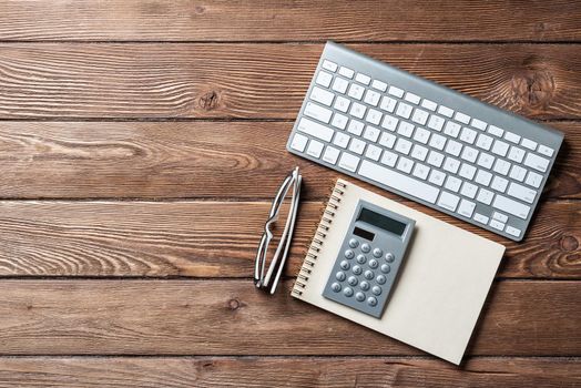 Still life of accountant workspace with office accessories. Flat lay wooden desk with computer keyboard, calculator and notepad. Accounting and banking services. Finance and investment concept.