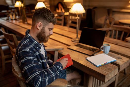 Casual business man or freelancer planning his work on notebook, working on laptop computer with smart phone, cup of coffee on table at coffee shop or home office, working from cafe concept