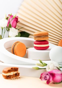 Beautiful festive composition macaron or macaroon cookies with white circles and flowers on beige background, colorful almond small cakes, Birthday, Mothers day, Woman day greetings card