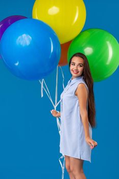 Smiling young woman looking camera and holding colorful air balloons isolated over blue. Conception of celebrations and birthday party