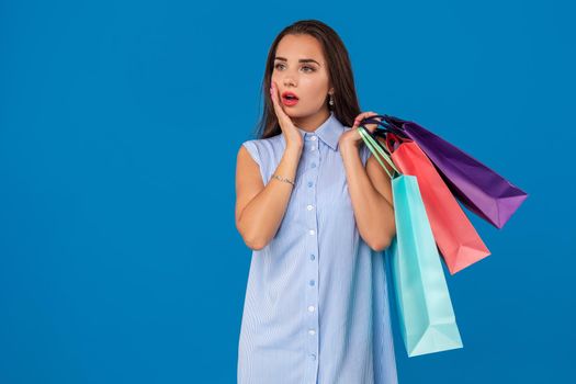 Photo of beautiful young woman with colorful shopping bags looking away on the wonderful blue background. The concept of shopping