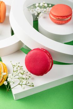 Beautiful festive composition macaron or macaroon cookies with white circles and flowers on green background, colorful almond small cakes, modern greetings card, selective focus