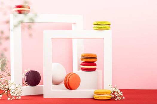 Colorful french macaron dessert. Set of various different tastes and color macaroon cookies with square shapes and flowers on pink background. Festive greeting card concept with copy space