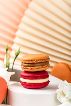 Beautiful festive composition macaron or macaroon cookies with white circles and flowers on beige background, colorful almond small cakes, Birthday, Mothers day, Woman day greetings card