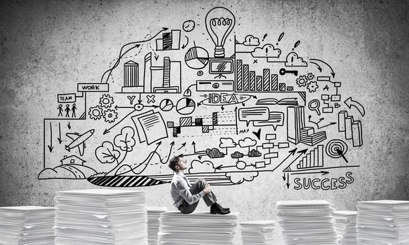 Businessman looking away while sitting on pile of documents against business-plan information on background. Mixed media.