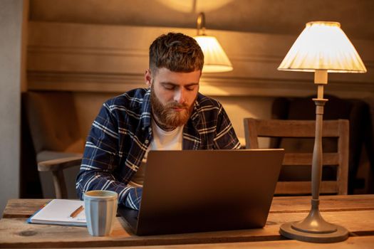 Young professional surfing the Internet on his laptop with cup of coffee on table at coffee shop or home office, working from cafe concept