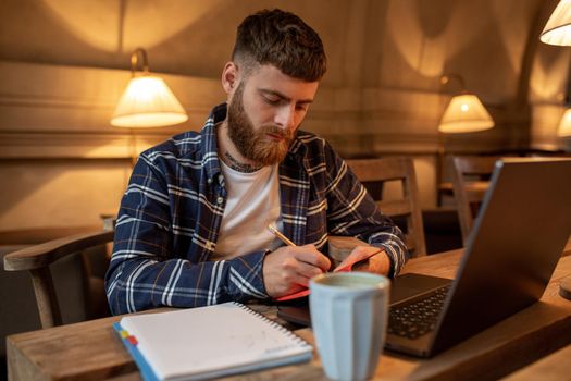 Casual business man or freelancer planning his work on notebook, working on laptop computer with smart phone, cup of coffee on table at coffee shop or home office, working from cafe concept