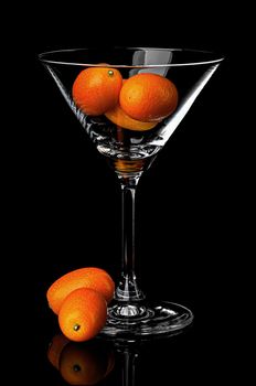 Ripe kumquat in martini glass on black background with reflection