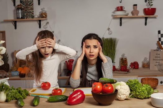 Happy loving family are cooking together. Lovely mum and her child are making a vegetable salad and tired of each other at the kitchen, against a white wall with shelves and bulbs on it. Homemade food and little helper.