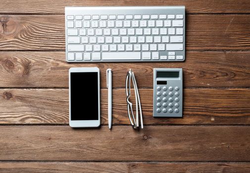 Top view of accountant workspace with office accessories. Flat lay wooden desk with computer keyboard, calculator and smartphone. Accounting and banking services. Finance and investment concept.