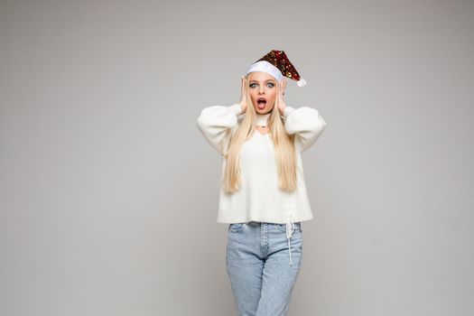 Close-up studio photo of a beautiful young lady in Santa hat cupping hands around mouth and making faces