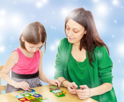 Cute little girl and her mother at the table laid out cards with pictures.Blue Christmas festive background with white snowflakes.