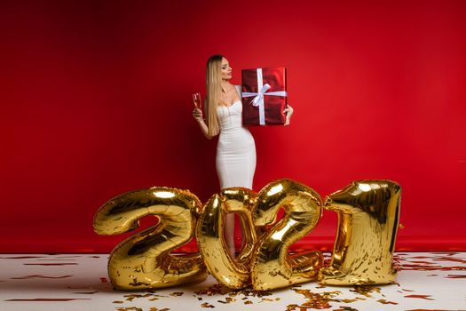 cheerful caucasian young woman in white dress holds a big red box with a gift, picture isolated on red background