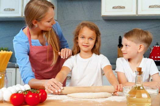 Mother and her little kids, boy and girl, helping her to prepare dough close up