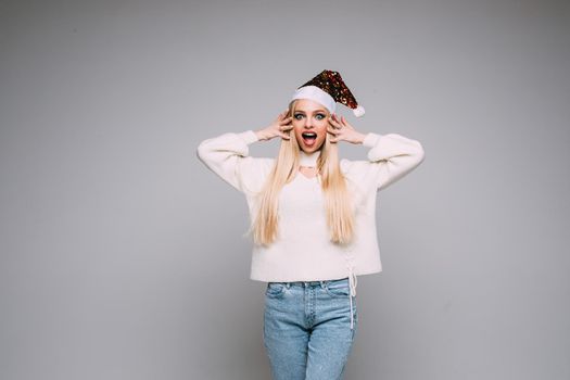 Portrait of pretty young lady in a white sweater celebrating the New Year, isolated on grey background. Holiday concept