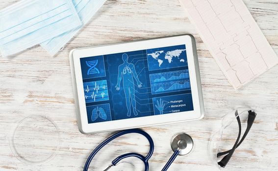 Modern social health insurance program. Tablet computer with healthcare application interface on screen. Stethoscope, x-ray image and cardiogram on wooden desk. Digital healthcare technologies.