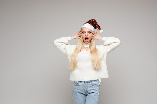 scared caucasian female with long fair hair in white sweater, blue jeans and red christmas hat