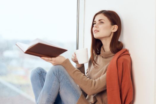 woman with a book near the window with a cup of coffee. High quality photo