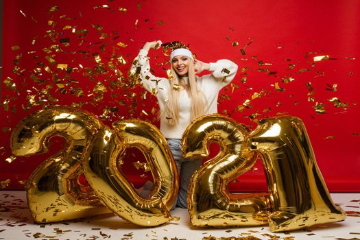 cheerful caucasian young woman in white sweater, blue jeans and red christmas hat with a lot of confetti, picture isolated on red background