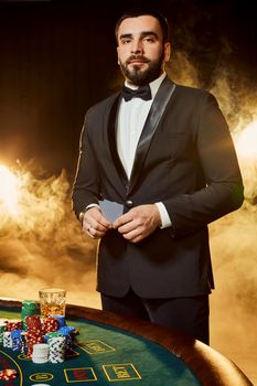 A young man in a business suit standing near poker table. Man gambles. The player at the gaming table playing cards.