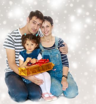 Happy young family with little daughter cuddling together in celebration of Christmas.Gray background with round white snowflakes.