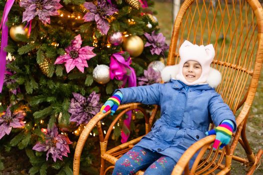 little girl in rocking chair near christmas tree on the street