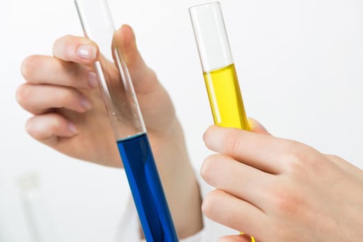 Clinic laboratory analysis and examination. Coronavirus disease testing. Closeup female hands holding test tubes with color liquid. Laboratory assistant comparing biological samples in test tubes.