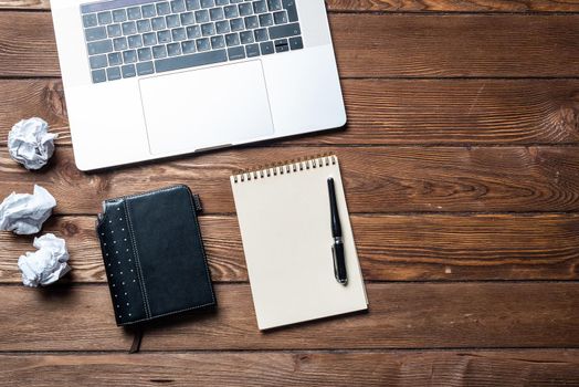 Still life of modern office workspace with supplies. Flat lay grunge wooden desk with laptop computer, diary and notepad with pen. Time management and day planning. Corporate business concept.