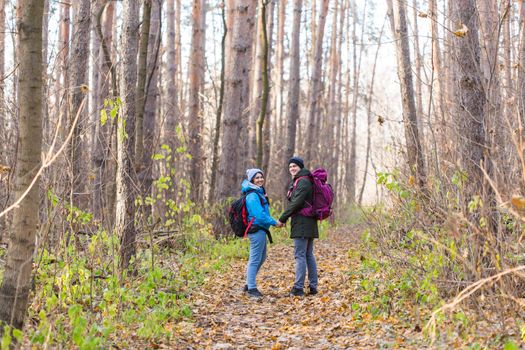 Travel, tourism, hike and nature concept - Tourists walking in park with backpack dressed in blue and black jackets.