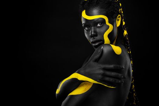 Face art. Woman with black and yellow body paint. Young african girl with colorful bodypaint. An amazing afro american model with yellow makeup.