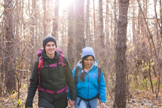 People, hike, adventures, tourism and nature concept - Young woman and man walking in forest with backpack.