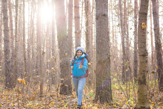 adventure, travel, tourism, hike and people concept - smiling tourist woman walking with backpacks over autumn natural background.