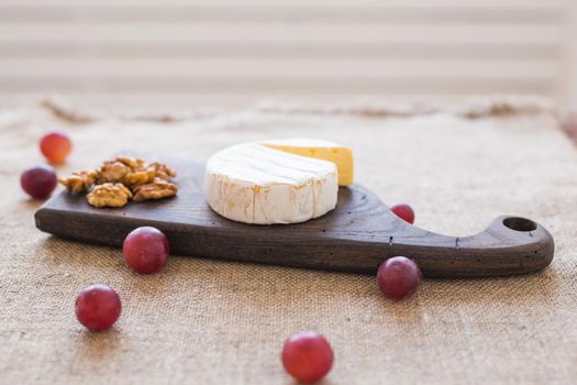 Brie or camembert cheese with nuts and grapes on a wooden board.