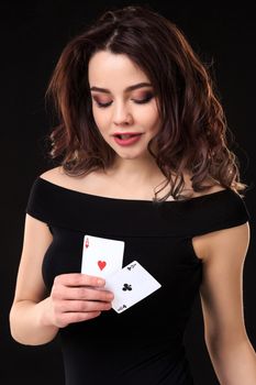 Young woman playing in the gambling on black background. Sexy brunette in a dress with two aces in her hand
