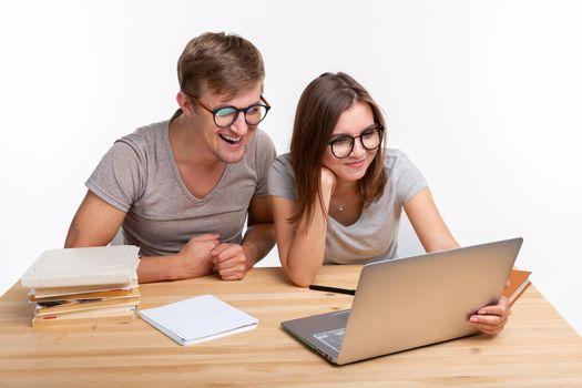 People and education concept - Two happy funny students sitting at the wooden table with laptop and books.