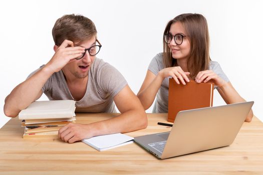 People and education concept - Two happy funny students sitting at the wooden table with laptop and books.