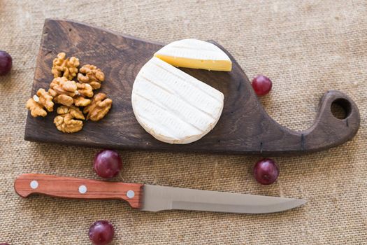 Brie or camembert cheese with nuts and grapes on a wooden board.