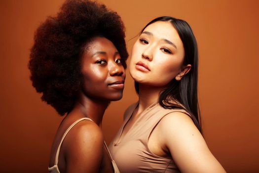 young pretty asian, afro woman posing cheerful together on brown background, lifestyle diverse nationality people concept close up