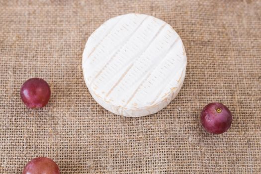 Brie or camembert cheese with grapes on rustic background.