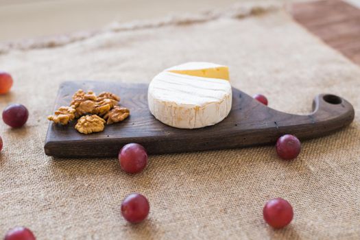Brie type of cheese. Camembert cheese. Fresh Brie cheese on a wooden board with nuts and grapes. Italian, French cheese