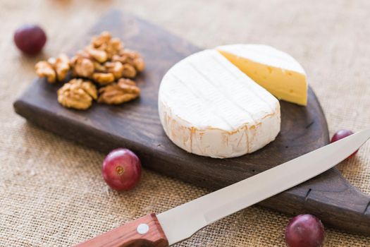 Brie type of cheese. Camembert cheese. Fresh Brie cheese on a wooden board with nuts and grapes. Italian, French cheese