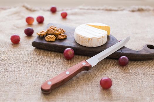 Brie type of cheese. Camembert cheese. Fresh Brie cheese on a wooden board with nuts and grapes. Italian, French cheese