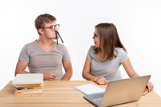 Education, fun and people concept - a couple of young people in glasses look like they are bored of learning homework and guy is making a stupid jokes, girl is laughing at him