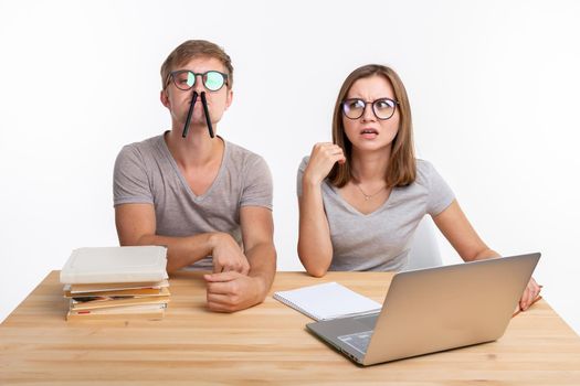 Education and people concept - a couple of young people in glasses look like they are bored of learning homework and make a stupid jokes.