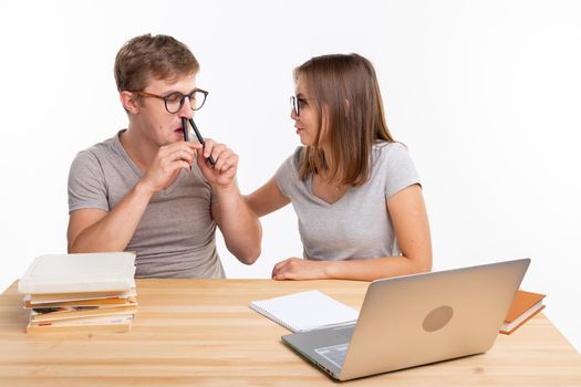 Education, fun and people concept - a couple of young people in glasses look like they are bored of learning homework and guy is making a stupid jokes, girl is laughing at him