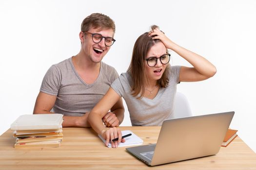 People and education concept - Two happy funny students sitting at the wooden table with laptop and books.